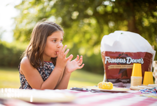 Girl licking her fingers sitting at a picnic table eating Famous Dave's BBQ