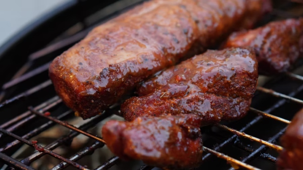 A savory hunk of meat lathered in BBQ sauce slow cooks on a grill.