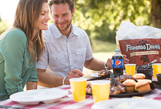 Man and woman sitting at a picnic table smiling and eating Famous Dave's BBQ
