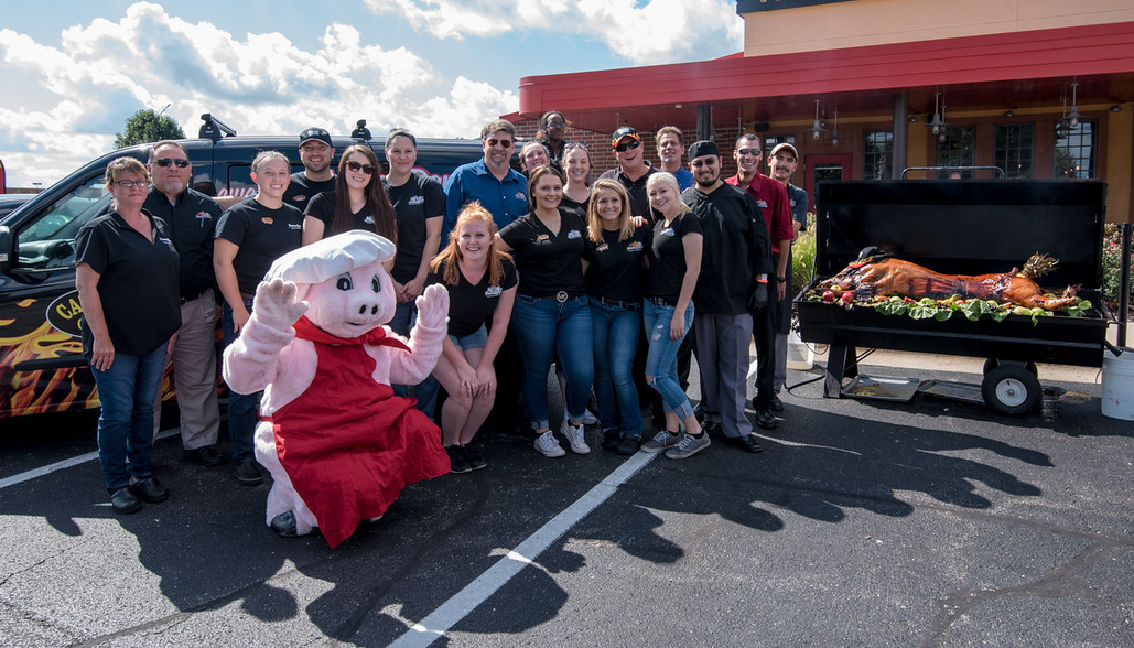 Famous Dave's BBQ Chicago employees standing with pig mascot in front of catering van