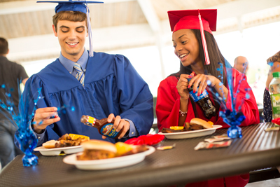 Two graduates at a graduation party eating Famous Dave's BBQ at a wood table