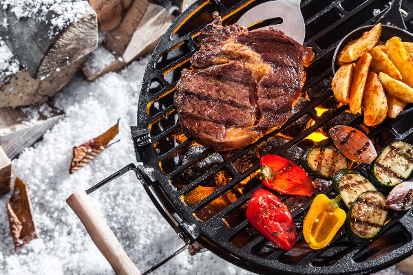 A cook grills food outside with snow on the ground.